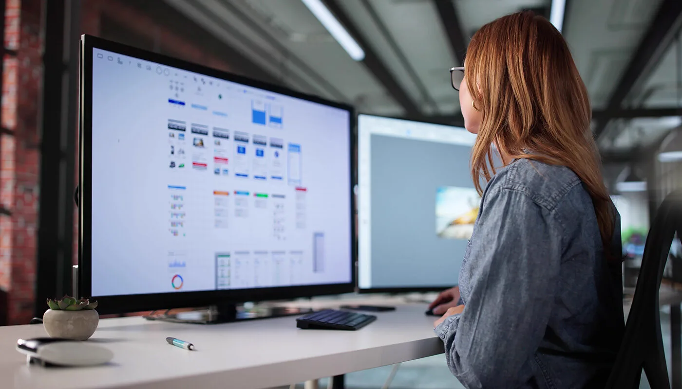 A young woman working as a freelance mobile app and UI designer, focused on her laptop while collaborating online in a modern workspace.